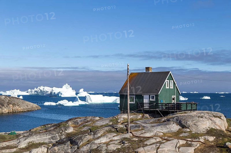 Qeqertarsuaq, Greenland, July 05, 2018: A green wooden house with icebergs in the background, North America