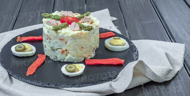 Black slate plate with ensaladilla rusa or Russian salad typical spanish tapa garnished with red bell pepper, hard boiled egg and asparagus