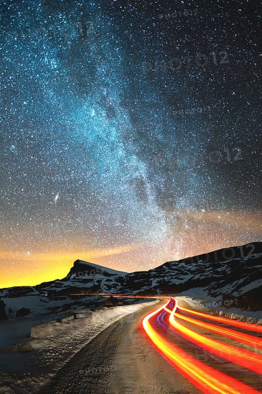 Night landscape. Night sky with a north hemisphere Milky Way and stars. The night road illuminated by the car winds with a serpentine and leaves in a distance to a foot of an acute rock. Light trails of red color. The concept of the path to knowledge and