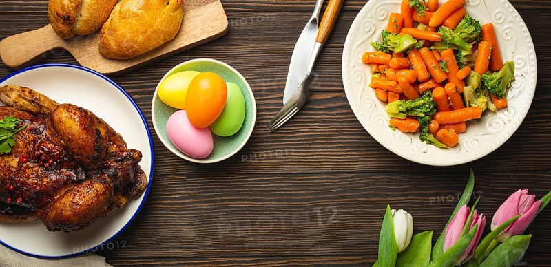 Easter food on dark rustic table: pastel colored eggs, roasted chicken and vegetables, buns and spring flowers tulips top view flay lay, Easter family dinner meal with festive dishes, space for text