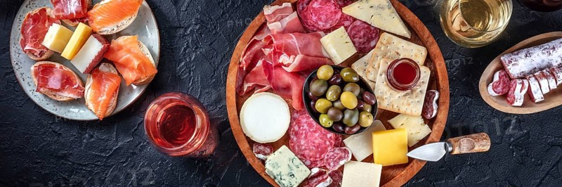 Italian antipasti or Spanish tapas panorama on a black background. Gourmet cold meat and cheese platter on a black background, shot from the top with wine. A variety of appetizers