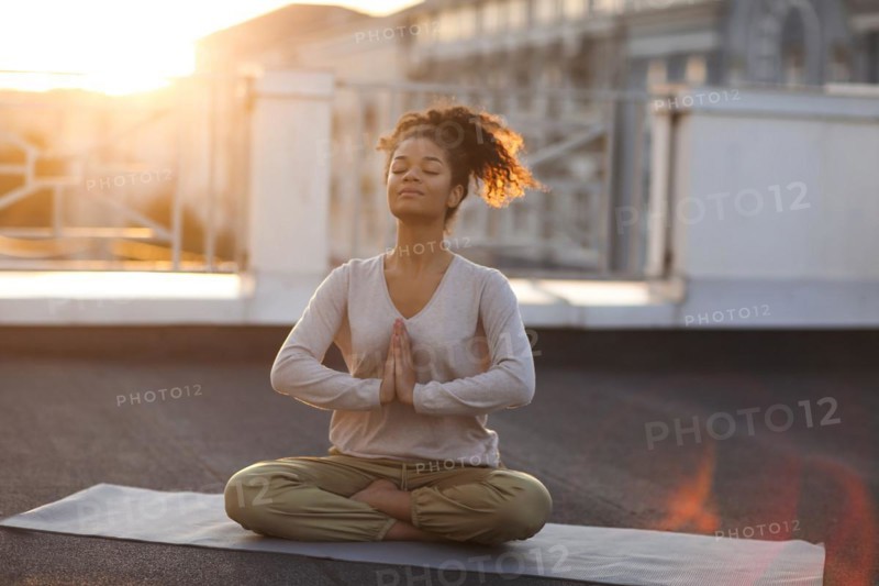 Cropped photo of woman sitting in lotus pose on mat and practicing yoga, female doing namaste gesture while meditating indoors. Meditation and mindfulness concept