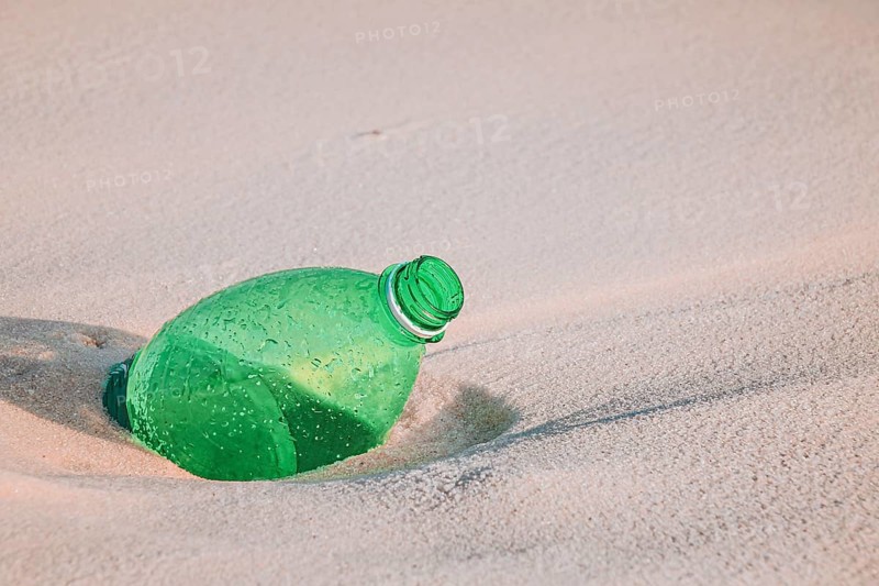 Green plastic bottle on sandy beach highlighting environmental pollution