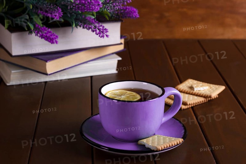 Cup of tea with lemon and cookies next to old books over vintage wooden background