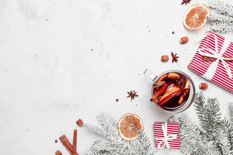 Christmas flat lay top view on white gray concrete background table with glass cup or mug of Mulled Wine, present red gift boxes, decorations, cinnamon sticks, hazelnut, dried or sublimated orange