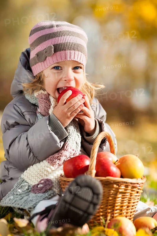 Happy kid eating red apple in autumn park. Healthy lifestyles concept
