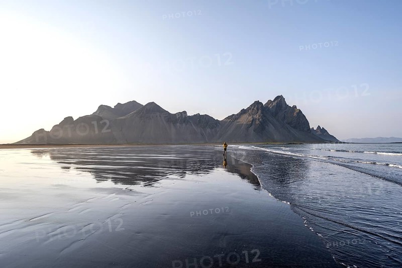 Tourist at black lava beach, sandy beach and sea, mountains Klifatindur reflected in the water, Eystrahorn and Kambhorn, headland Stokksnes, mountain range Klifatindur, Austurland, East Iceland, Iceland, Europe