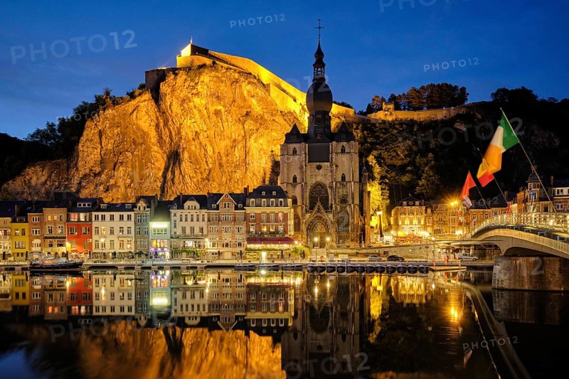 Night view of Dinant town, Collegiate Church of Notre Dame de Dinant over River Meuse and Pont Charles de Gaulle bridge and Dinant Citadel illuminated in the evening. Dinant, Belgium, Europe