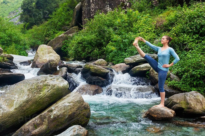 Yoga outdoors, woman doing Ashtanga Vinyasa Yoga balance asana Utthita Hasta Padangushthasana, Extended Hand-To-Big-Toe Pose position posture outdoors at waterfall