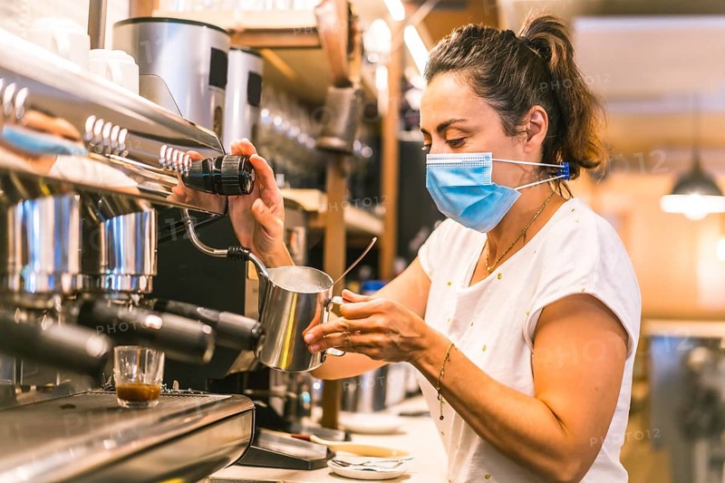 A waitress with a face mask in a bar. New normality, security measures after the coronavirus pandemic, social distance, covid-19. Preparing a coffee