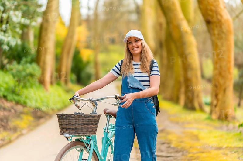 Young woman walking alongside her bicycle in a vibrant park, soaking up the warmth of a sunny day while enjoying the beauty of nature