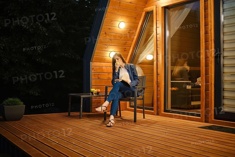 Late in the evening, a young woman sits on the terrace of a country house, eats an apple and reads a book