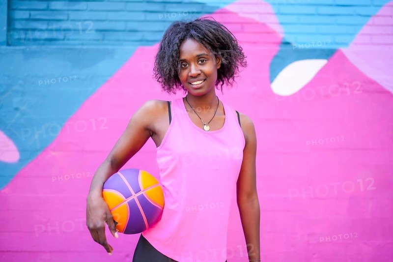 Portrait of a happy african female basketball player against colorful urban wall
