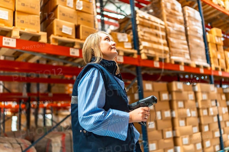 Blonde woman manual worker in waistcoat scanning parcels in a warehouse