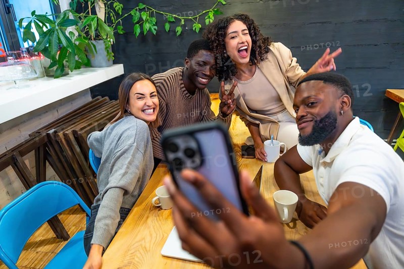 African man taking selfie with diverse colleagues in the cafeteria of a coworking