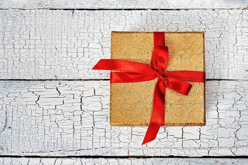 Gift birthday Christmas present concept, yellow gold gift box with red ribbon on white painted wooden background. Top view