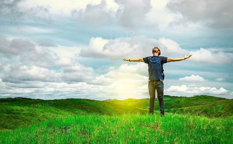 Adventurous man spreading his arms in the countryside. Man with backpack on a hill spreading his arms. Explorer man spreading his arms on a hill. Lifestyle of adventurous man in the field