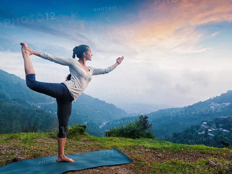 Woman doing yoga asana Natarajasana, Lord of the dance pose outdoors at waterfall in Himalayas