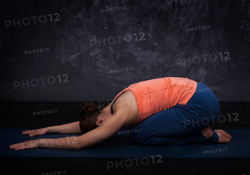 Beautiful sporty fit yogini woman practices yoga asana balasana (child's pose), resting pose or counter asana for many asanas on dark background
