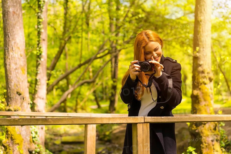 Woman photographer with a black jacket enjoying in an autumn park, smiling and enjoying taking photos at sunset