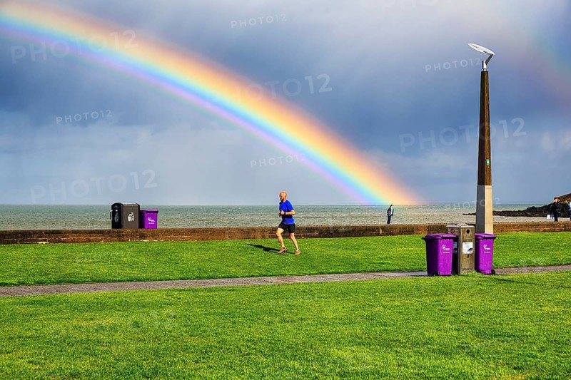 Pedestrians and joggers on seafront promenade, dramatic cloudy sky with rainbow, Bray, Wicklow, Ireland, Europe