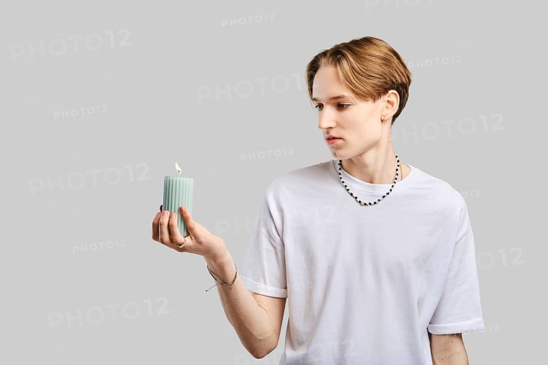 Young man holds candle in hand over grey studio background