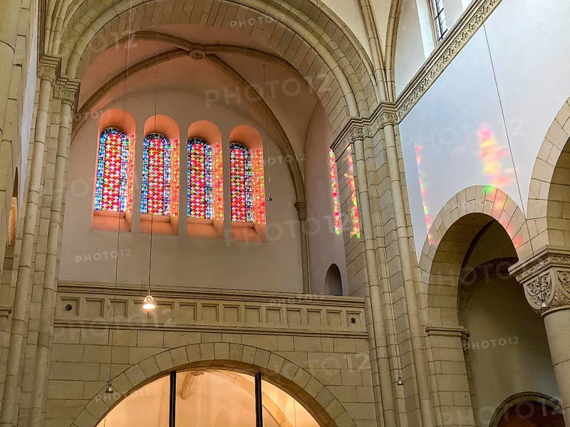 Sun shines through four stained glass windows above main portal of Benedictine Abbey Gerleve casts colourful light into nave, Gerleve, Münsterland, North Rhine-Westphalia, Germany, Europe