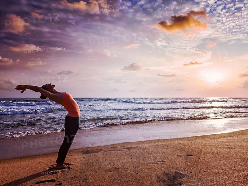 Vintage retro effect hipster style image of young sporty fit woman doing yoga Sun salutation Surya Namaskar pose Hasta Uttanasana on tropical beach on sunset