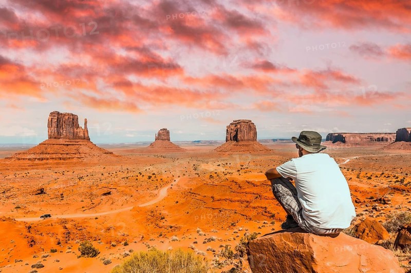 A young boy with white t-shirt sitting in the center of the photo on a stone in the Monument Valley National Park in the visitor center. Utah