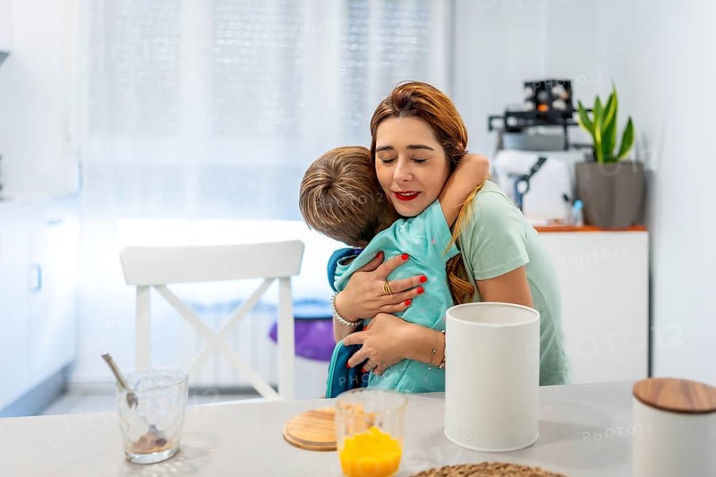 Happy moment of a caucasian school boy embracing her mother while eating breakfast at home