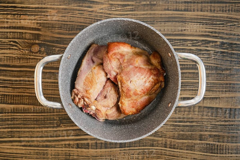 Tender, cooked turkey meat sit in a silver pot on a rustic wooden table, showcasing their golden brown exterior. The kitchen atmosphere highlights a cozy, home-cooked meal vibe.