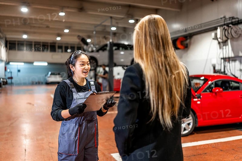 Smiling female mechanic explaining repair details to a customer while delivering a car in a modern auto repair shop
