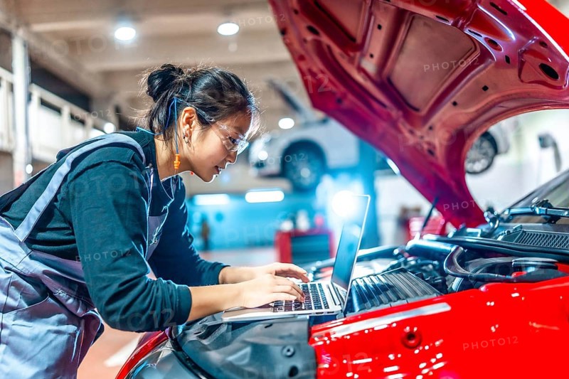Young female mechanic using a laptop while performing diagnostics on a red car in a modern auto repair shop
