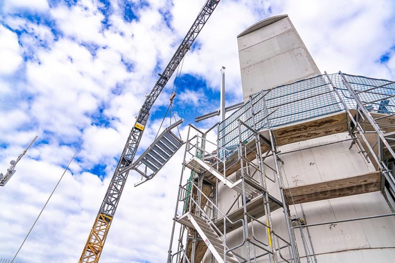 Construction crane lifts staircase structure next to tower and scaffolding in front of a cloudy sky, staircase extension to the new tower of the Calw railway station on the new track of the Hermann Hessebahn, Calw, Black Forest, Germany, Europe