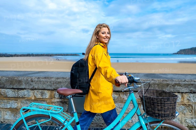 Tourist walking with her bicycle along the beach wall on a cloudy day, enjoying the fresh air and scenic views