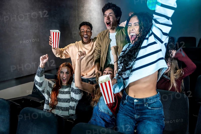 Excited friends cheering together during a movie night at the cinema, enjoying popcorn and sharing joyful moments in the darkened auditorium