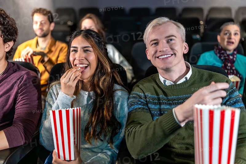 Young couple enjoying a movie at the cinema, eating popcorn and smiling, surrounded by other people