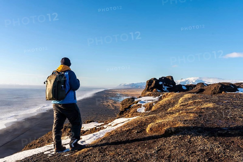 A tourist man with his back turned at the viewpoint of Dyrholaey beach in the cold winter with snow in Iceland