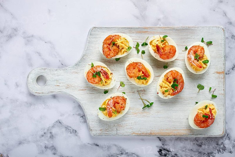 Boiled eggs stuffed with yolk and seasoned with mayonnaise, stuffed eggs with shrimp, on a white wooden chopping board, selective focus, close-up, without people