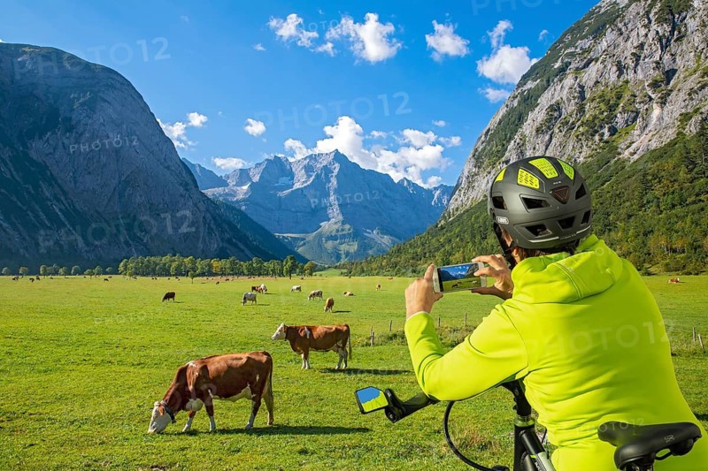 A biker uses her mobile phone to photograph the Großer Ahornboden and the grazing cows, Großer Ahornboden, Karwendel Mountains, Tyrol, Austria, Europe