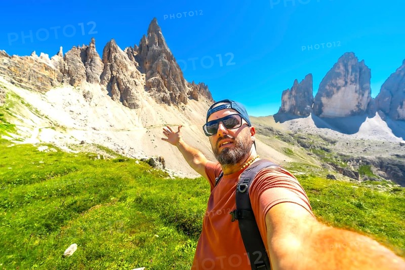 Hiker taking a selfie with the tre cime di lavaredo in the background, during a summer hike in the dolomites
