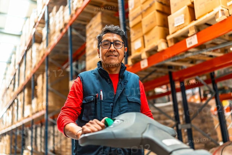 Low angle view portrait of a cheerful latin warehouse worker using machinery