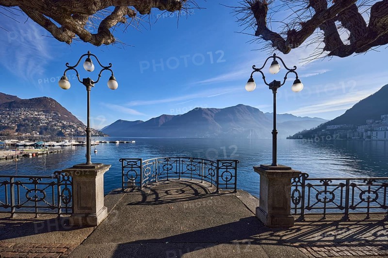 Lake, lakeside promenade, lanterns, trees, railings, mountains, haze, shadow, backlight, Lake Lugano, Lugano, Lugano district, Canton Ticino, Switzerland, Europe
