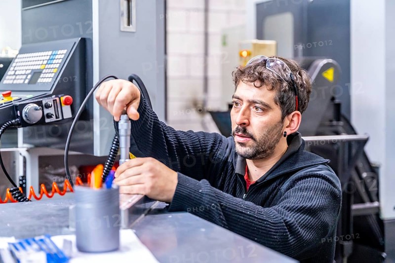 Concentrated engineer crouching fixing a piece of metal in a cnc modern factory