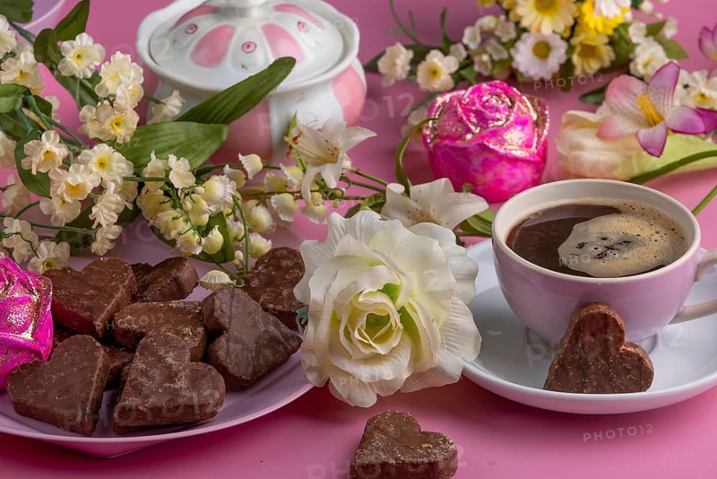 Coffee mug with heart-shaped chocolate and flowers on a pink background, Valentine's Day
