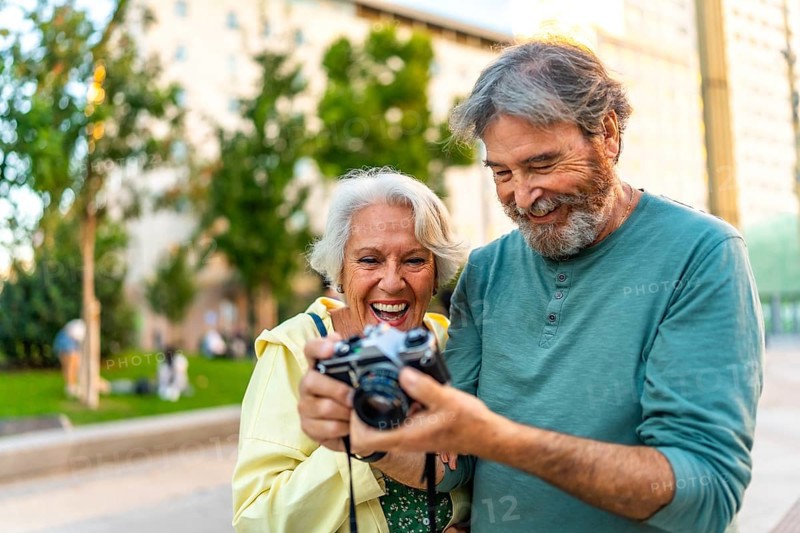 Happy senior couple looking at the photos in a camera standing in the city street