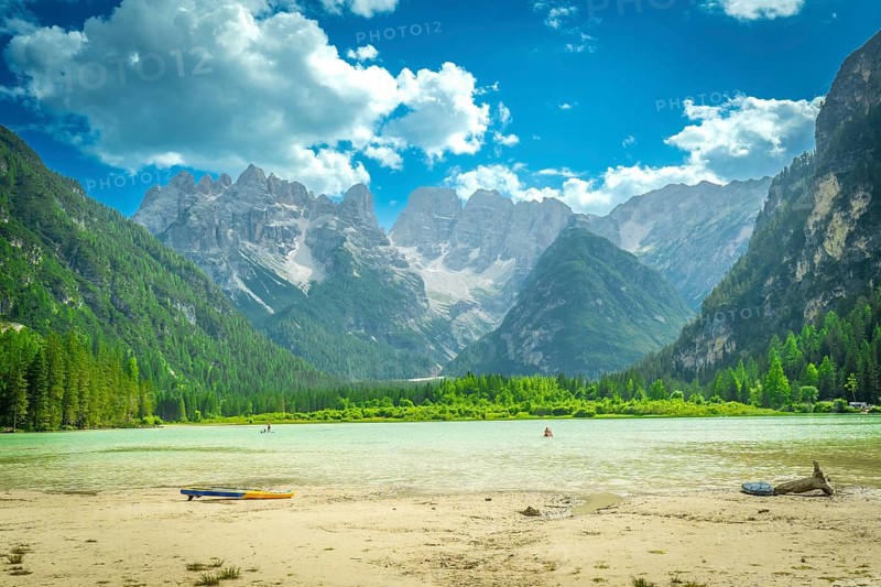 Tourists swimming and paddleboarding in the turquoise waters of lago di landro, surrounded by the breathtaking peaks of the dolomites on a sunny summer day