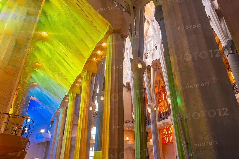 Sunlight illuminates colorful stained glass windows, casting vibrant hues onto architectural columns inside sagrada familia in barcelona