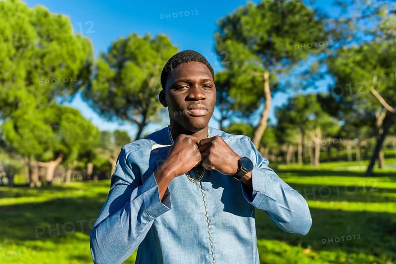 Young african man wearing traditional dashiki attire, adjusting his collar in a serene park setting