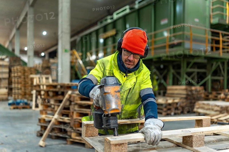 Man worker using compressed air gun to repair pallets in a recycling plant